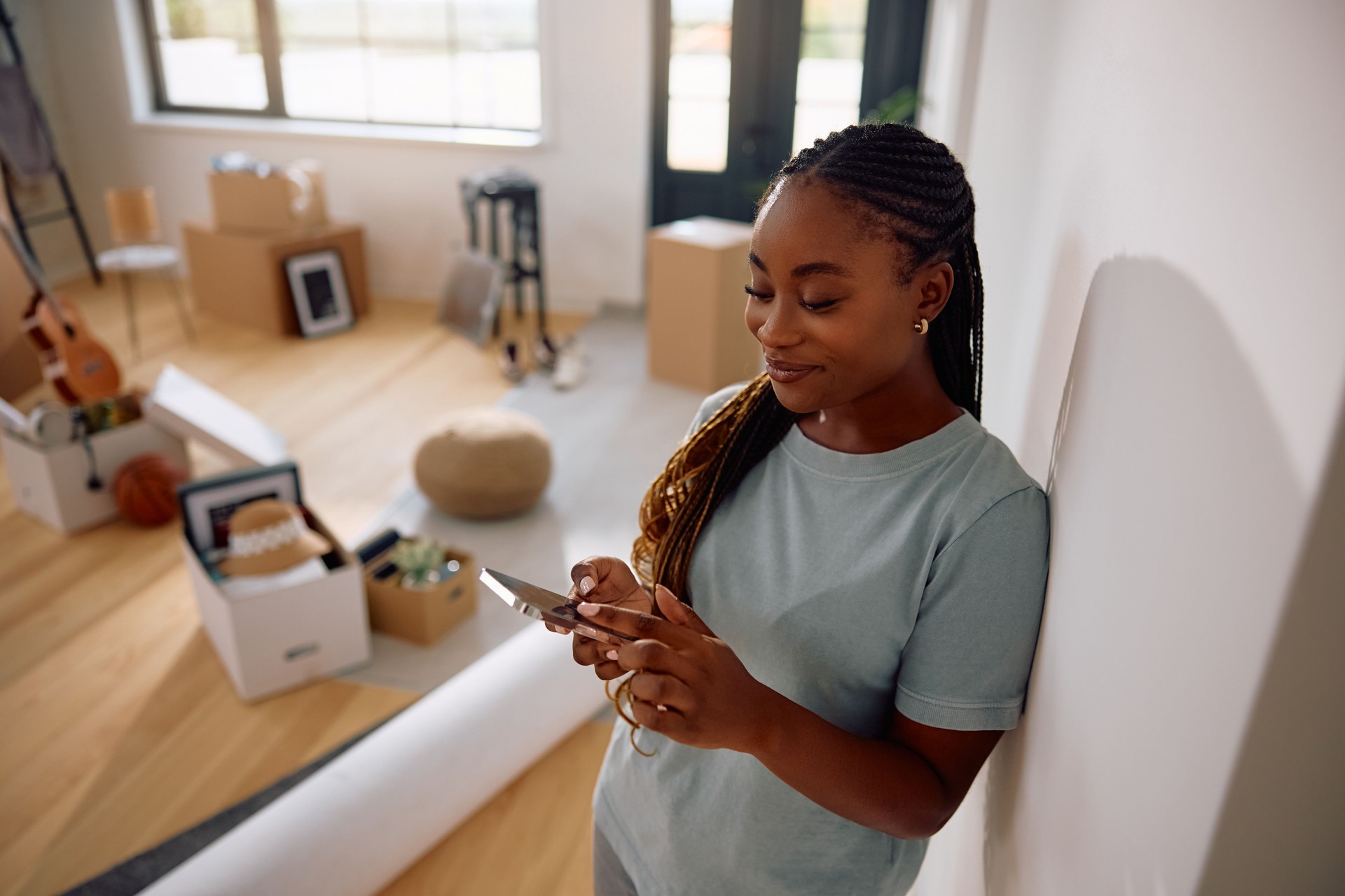 Happy black woman using mobile phone after moving into new home.